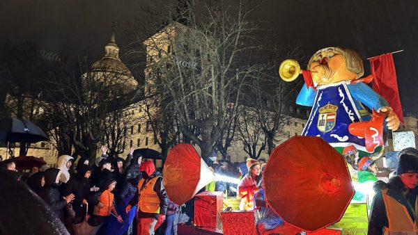 Una colorida carroza navideña con una gran figura de un paje real tocando una trompeta desfila de noche por San Lorenzo de El Escorial.