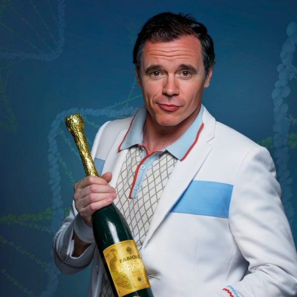 El actor Rafa Maza, caracterizado como su personaje Fabiolo, viste una chaqueta blanca con franja azul y sostiene una botella de champán dorada.