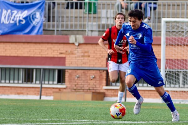 Un jugador de Las Rozas CF, vestido con equipación azul, conduce el balón con velocidad durante el partido contra el Unión Adarve.