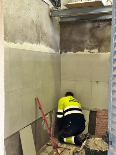 Personal de obra con chaleco amarillo reflectante poniendo baldosas largas en una habitación que está en obras.