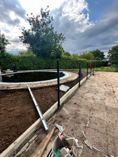 Vista de una piscina redonda y vacía, rodeada de tierra excavada y una acera de piedra. Se están realizando trabajos de reforma.