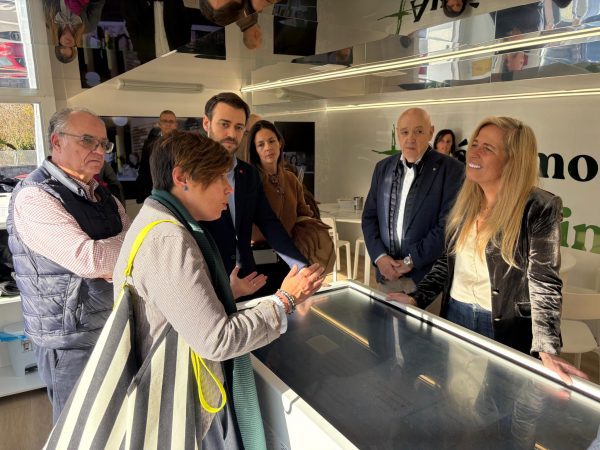 La consejera Rocío Albert y el alcalde José María Moreno, junto a otros miembros, interactuando con una mesa digital de información dentro del autobús de asesoramiento a emprendedores.