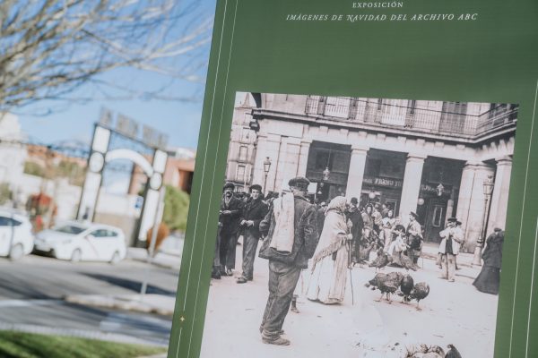 Primer plano del cartel de la Exposición al aire libre Imágenes de Navidad del Archivo de ABC en blanco y negro y al fondo una calle con un portalón de luces