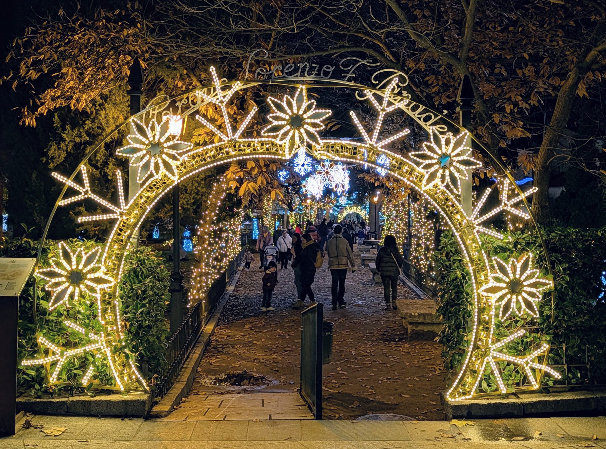 Arco de entrada al "Jardín de la Navidad" de El Escorial decorado con luces doradas en forma de copos de nieve gigantes y follaje.