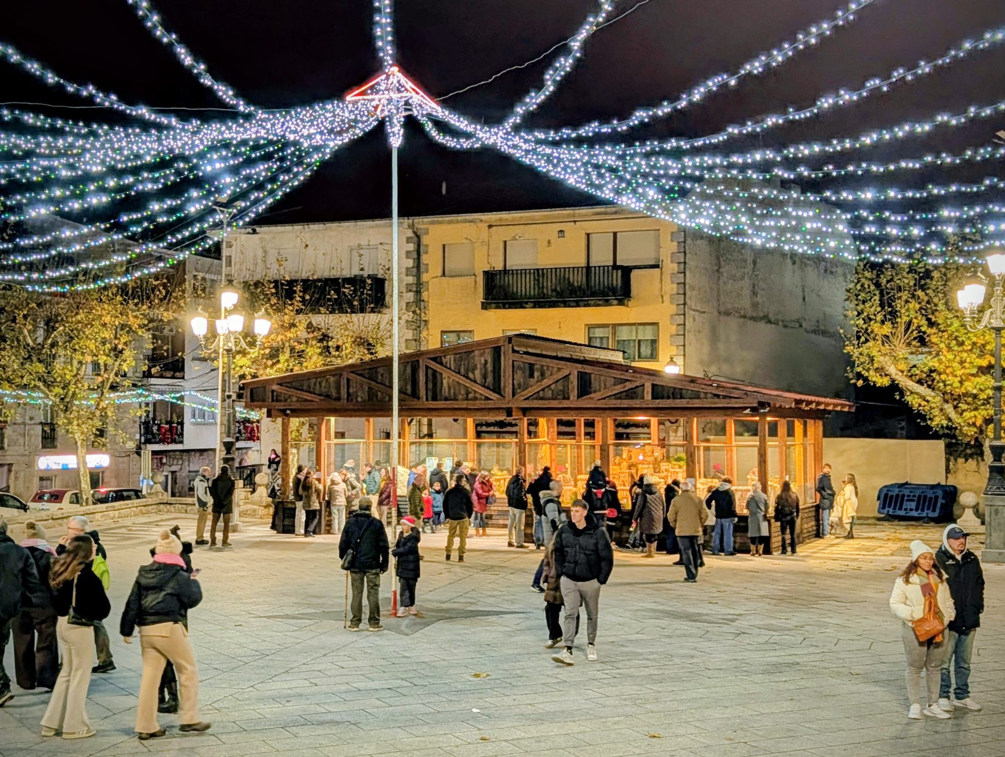 Plaza central de el Escorial con luces blancas y gente reunida alrededor de un pabellón de madera.