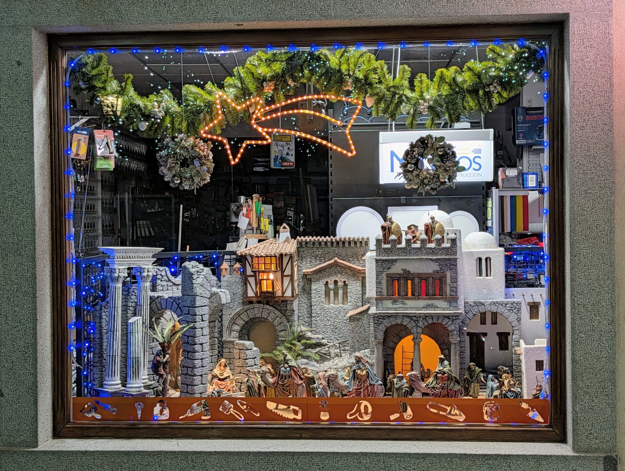 Escaparate con una compleja representación de un Belén o nacimiento, enmarcado con guirnaldas y luces azules.
