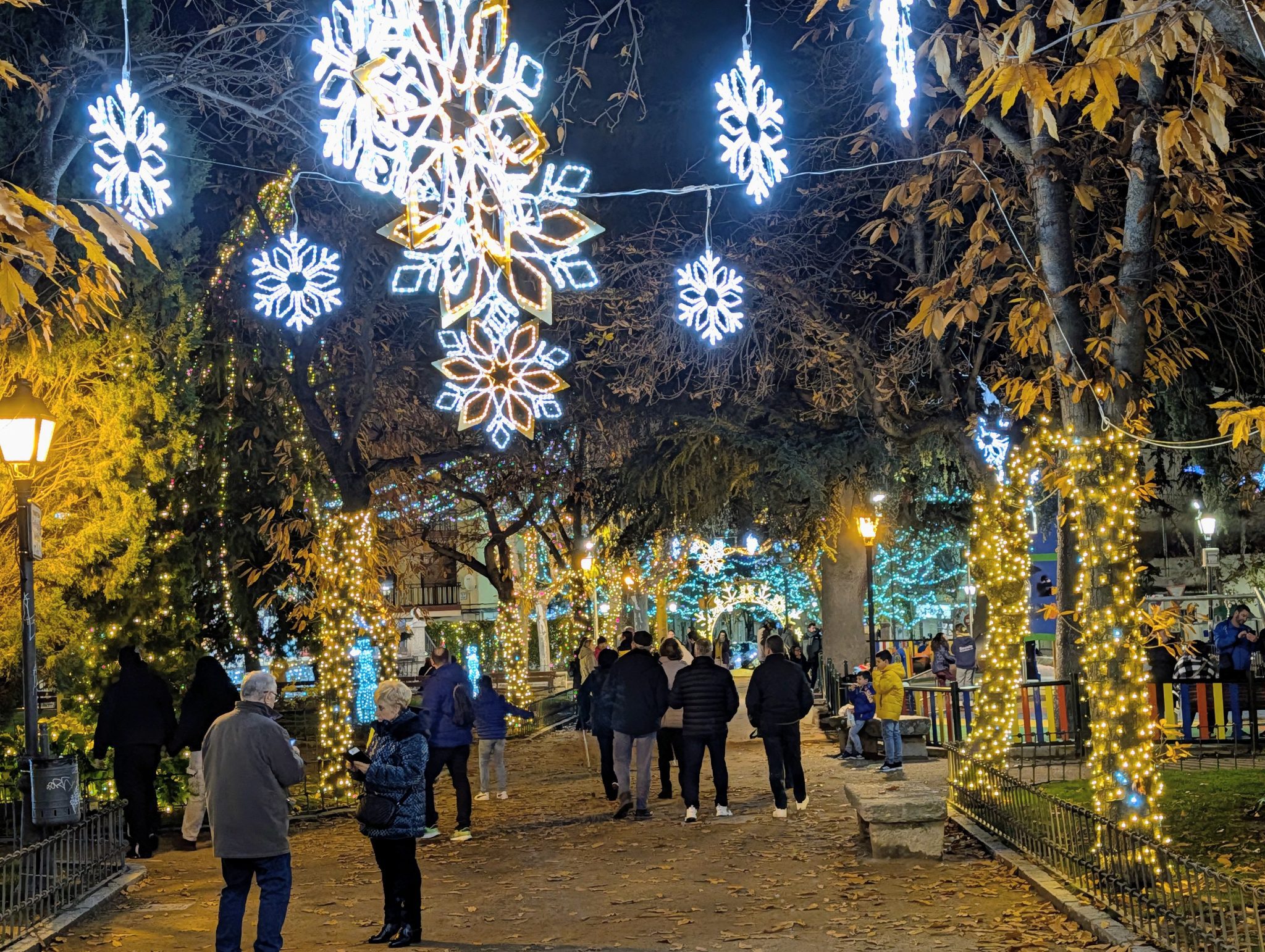 Paseo de un parque por la noche con grandes copos de nieve luminosos colgantes.