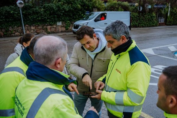 Plano cercano del alcalde de Las Rozas señalando una información en un dispositivo móvil mientras conversa con operarios y técnicos municipales a pie de obra.