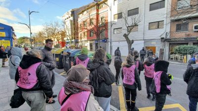 Vista general de la calle durante la concentración de protesta. Se observa a un grupo de personas de espaldas, algunas con chalecos rosas identificativos