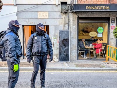Dos agentes de la Policía Local, con el rostro parcialmente cubierto, vigilan el exterior del portal 13-15 de la calle Real.