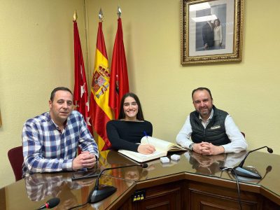 Dos representantes municipales junto a Iraide Rodríguez, sentados en una rueda de prensa frente a un fondo azul con logos del Ayuntamiento de Collado Villalba.