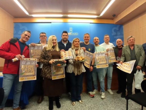 Un grupo de representantes municipales, hosteleros y organizadores posan sonrientes sosteniendo carteles promocionales de la "V Feria de la Tapa".