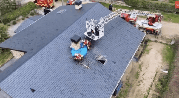 Vista aérea de bomberos trabajando sobre el tejado de una vivienda utilizando un camión autoescala para extinguir un incendio.