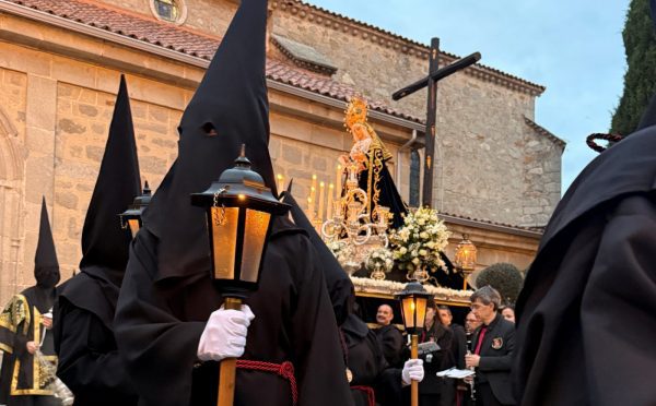 Penitentes con túnicas y capirotes negros portando faroles iluminados durante una procesión nocturna frente a la iglesia de Galapagar.