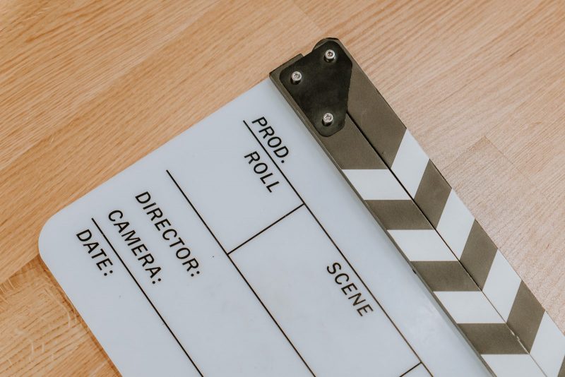 Primer plano detallado de una claqueta de cine blanca sobre un suelo de madera, con espacios en blanco para rellenar los datos de producción.