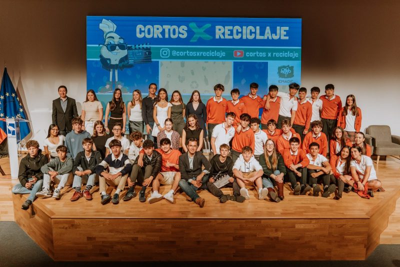 Gran grupo de estudiantes y representantes municipales posando sentados y de pie en el escenario de un auditorio tras la gala de presentación.