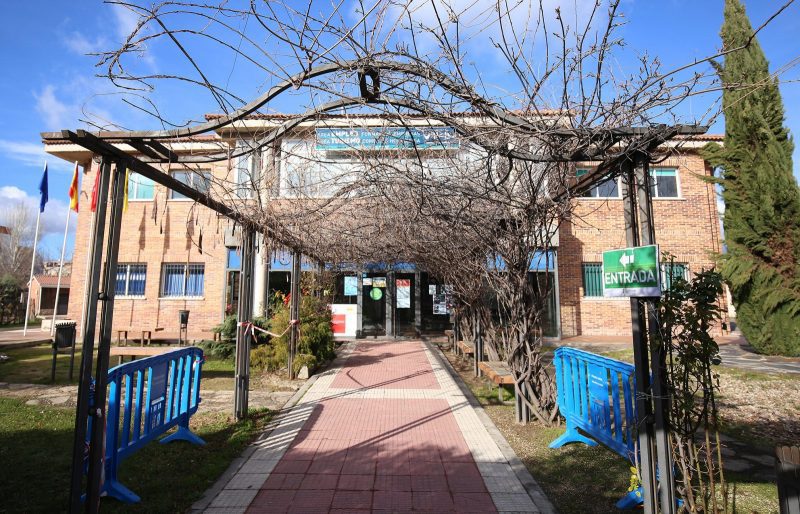 Fachada exterior de ladrillo del Centro de Iniciativas Municipales con un camino de acceso bajo una pérgola de ramas.