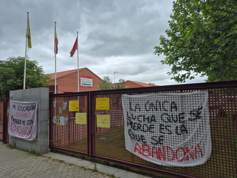 Valla metálica de una escuela con una pancarta blanca que dice: "La única lucha que se pierde es la que se abandona".