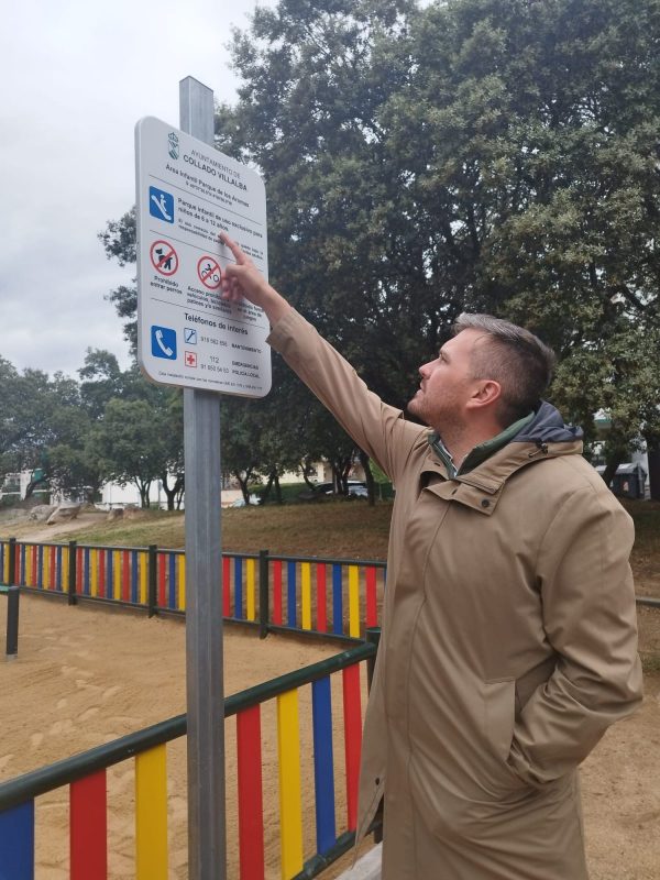 El concejal Adan Martínez señala un cartel informativo blanco instalado junto a la valla perimetral del parque.