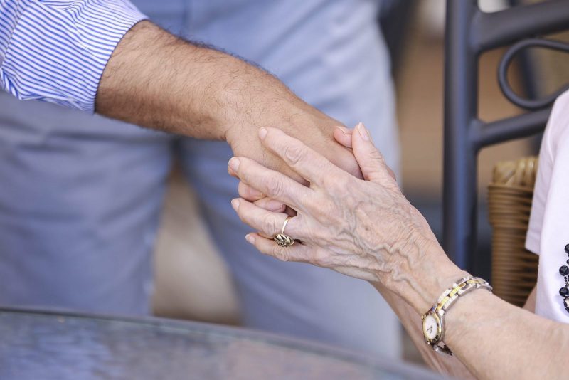 Primer plano de una mano de piel arrugada sosteniendo con delicadeza la mano de otra persona en un gesto de apoyo.