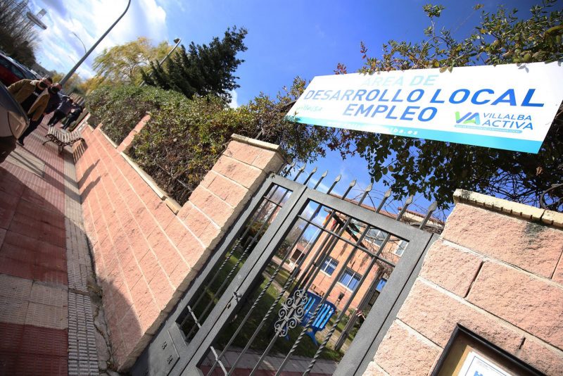 Un cartel azul y blanco que dice "ÁREA DE DESARROLLO LOCAL EMPLEO VILLALBA ACTIVA" sobre la puerta de entrada a un edificio.