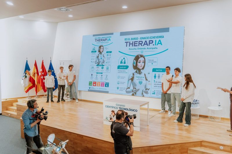 Varios jóvenes exponen en un escenario frente a una pantalla gigante con el proyecto de inteligencia artificial Therap.ia.