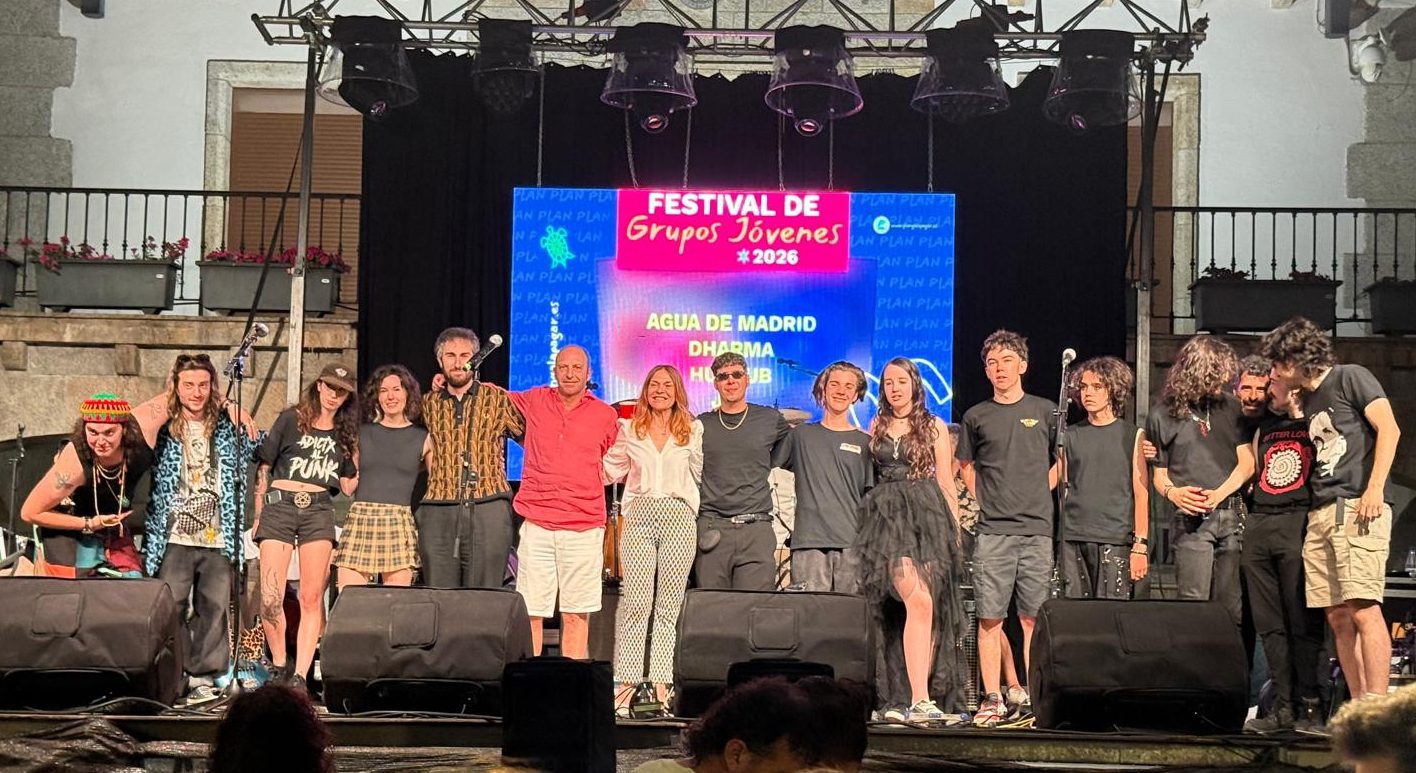 Grupo numeroso de personas posa abrazado sobre un escenario iluminado, frente a una gran pantalla con texto de un festival de música.