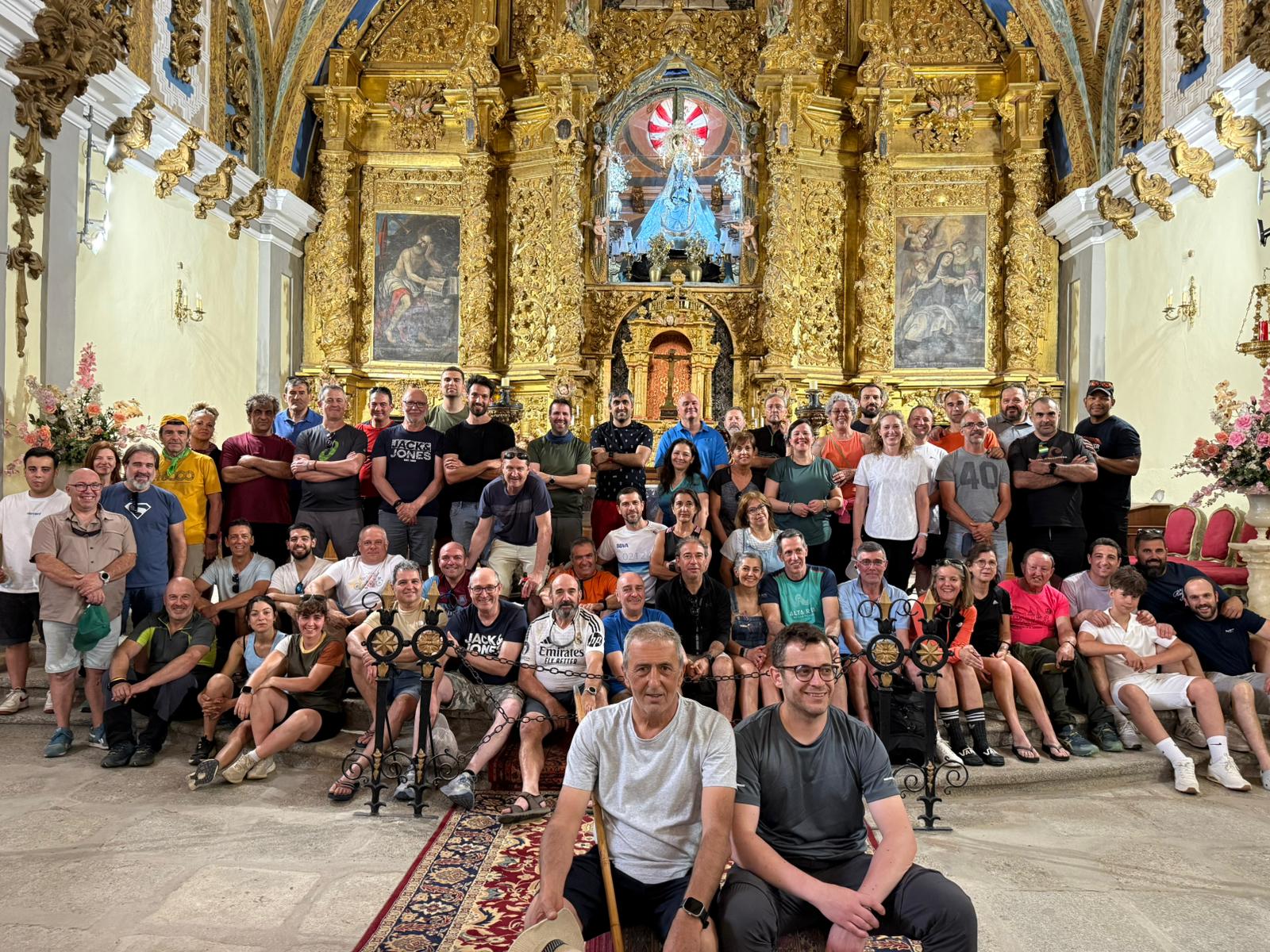 oto de grupo de los senderistas sentados y de pie frente al impresionante y dorado retablo barroco en el interior de una iglesia.