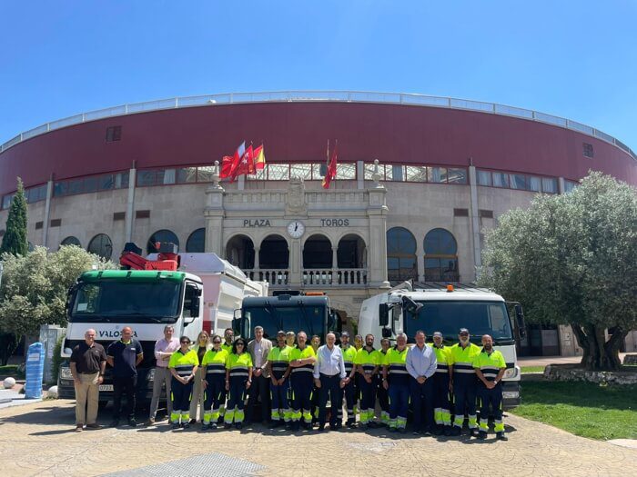 Un grupo de operarios y autoridades posa frente a tres camiones de limpieza, con la Plaza de Toros de fondo