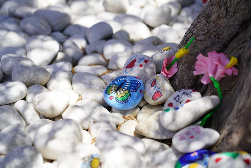 Detalle de piedras blancas sobre el suelo, algunas pintadas con dibujos de mariposas, corazones y mensajes de recuerdo.