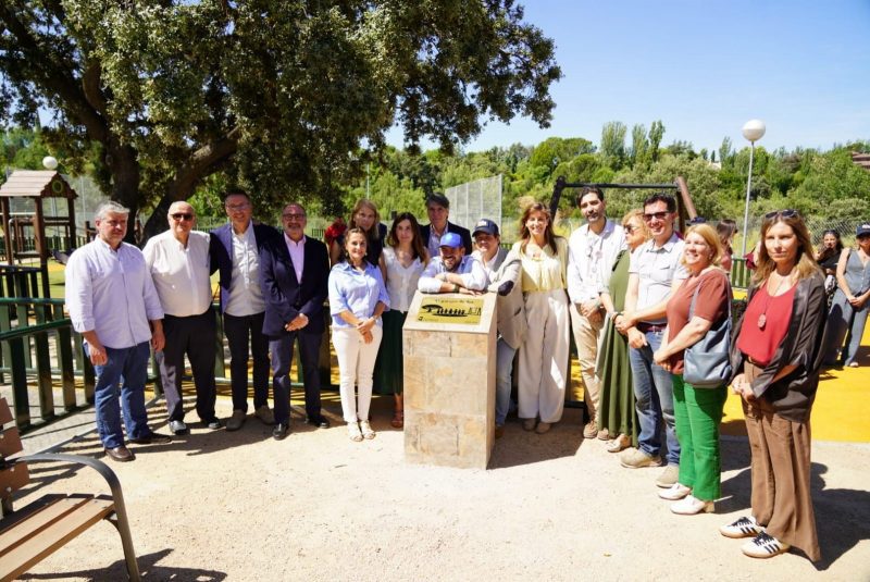 Autoridades y familiares posan junto a un monolito con una placa conmemorativa en un parque infantil al aire libre.