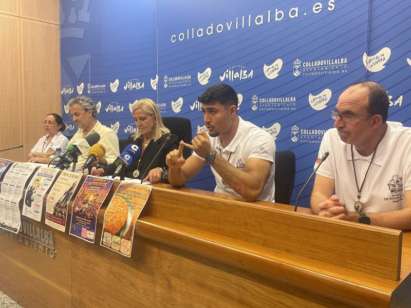 Cinco personas sentadas en una larga mesa de prensa con carteles festivos colgados en el frontal de madera.
