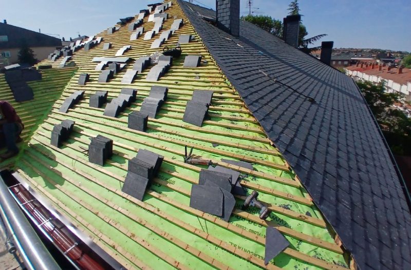Tejado en obras con una mitad cubierta de pizarras negras y la otra zona mostrando los listones de madera.