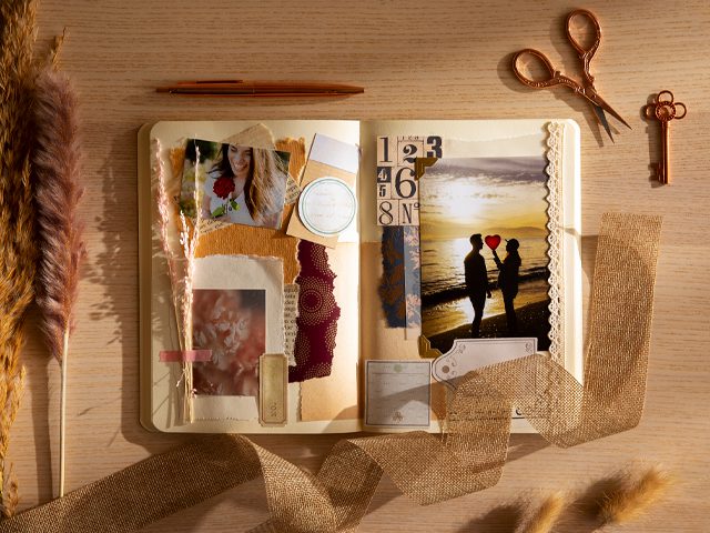 Un cuaderno abierto tipo scrapbook o álbum artesanal con fotografías, recortes de papel, una cinta de yute y tijeras doradas sobre una mesa.