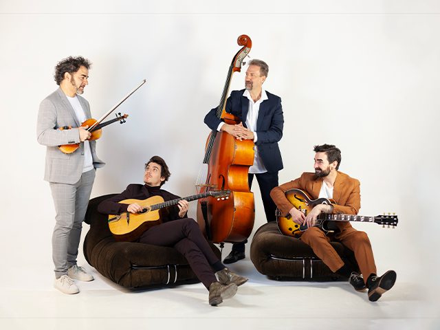 Cuatro músicos posan con instrumentos de cuerda: un violín, un contrabajo y dos guitarras, sobre un fondo blanco.