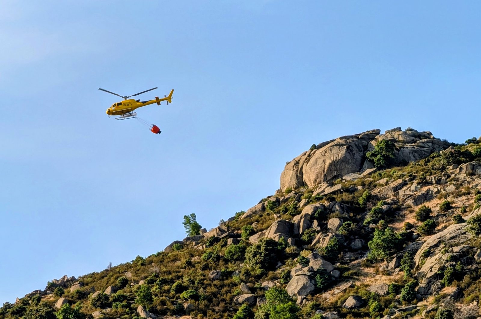 Un helicóptero del INFOMA pasa junto a la Machota Baja, en Zarzalejo