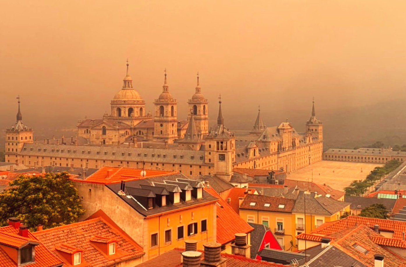Vista de San Lorenzo de El Escorial bajo un cielo anaranjado por el humo del incendio forestal.