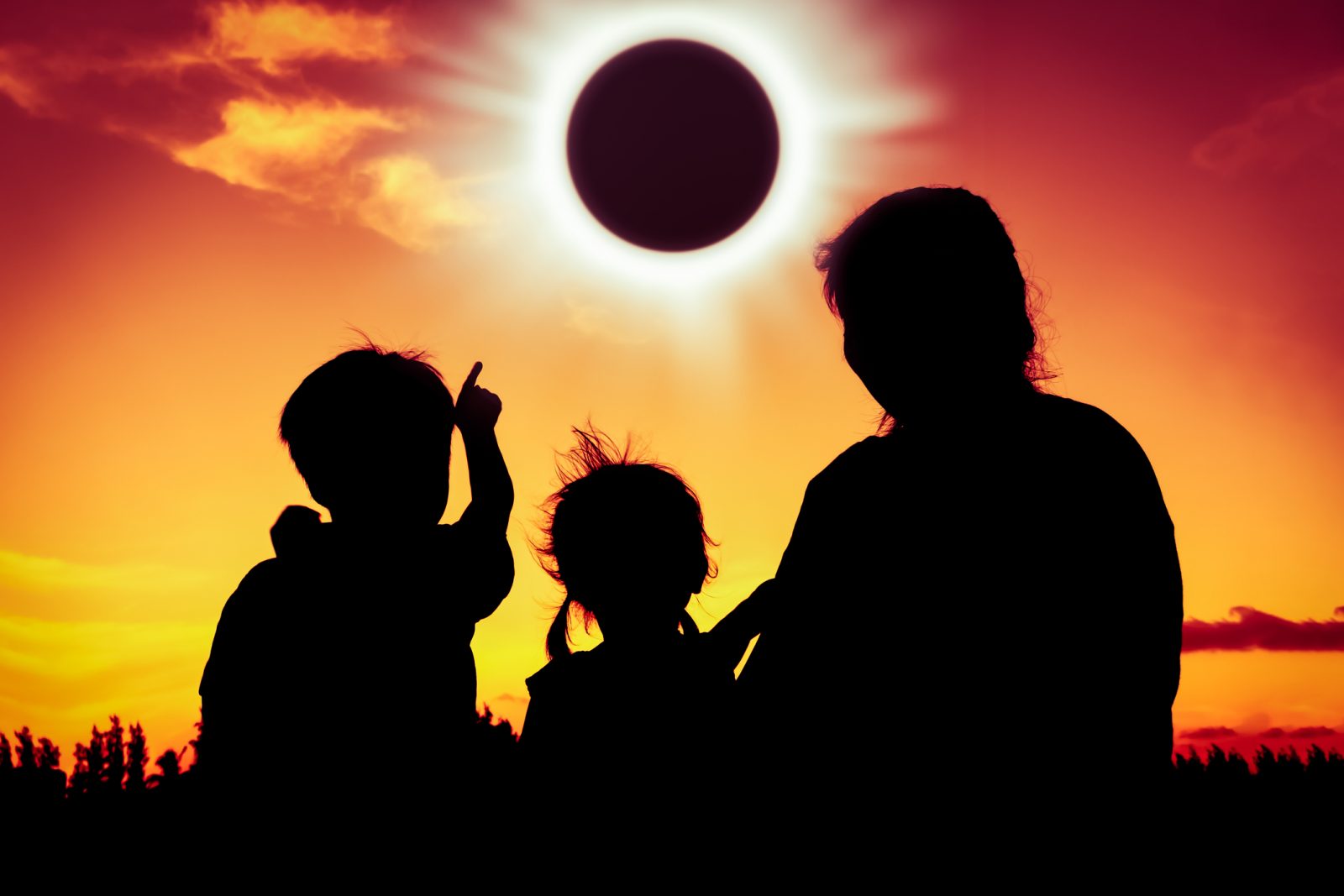 Silueta de personas observando un eclipse solar completo al atardecer.