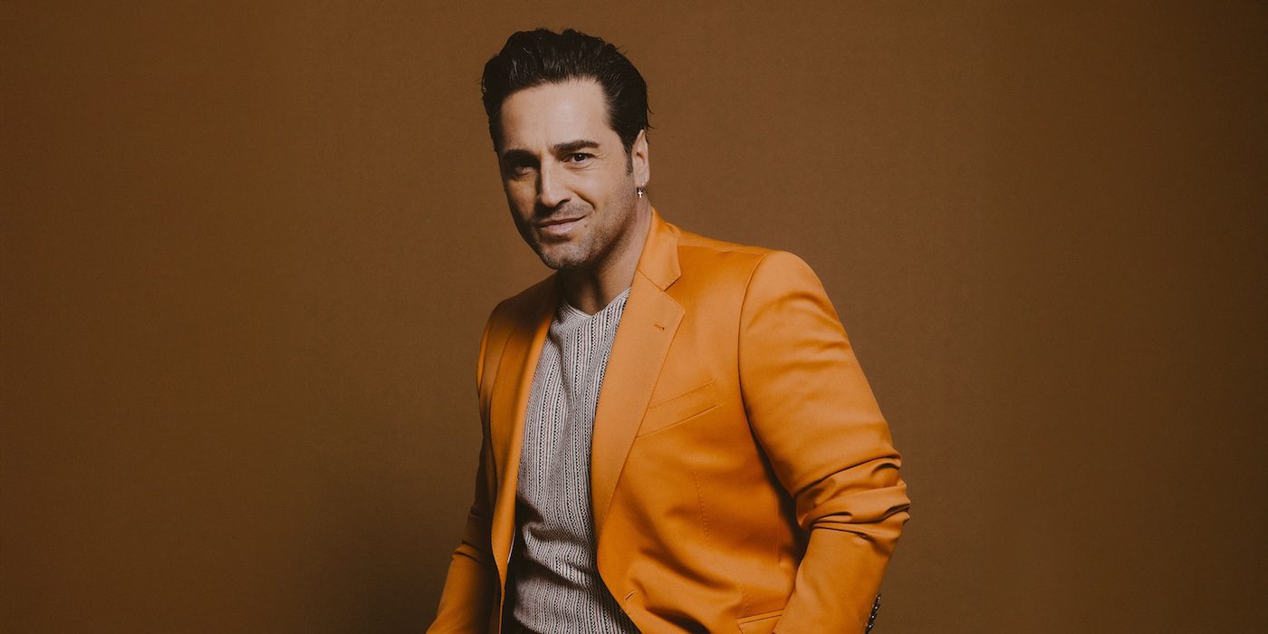 El cantante David Bustamante posa de medio cuerpo vistiendo una chaqueta naranja sobre un fondo café.