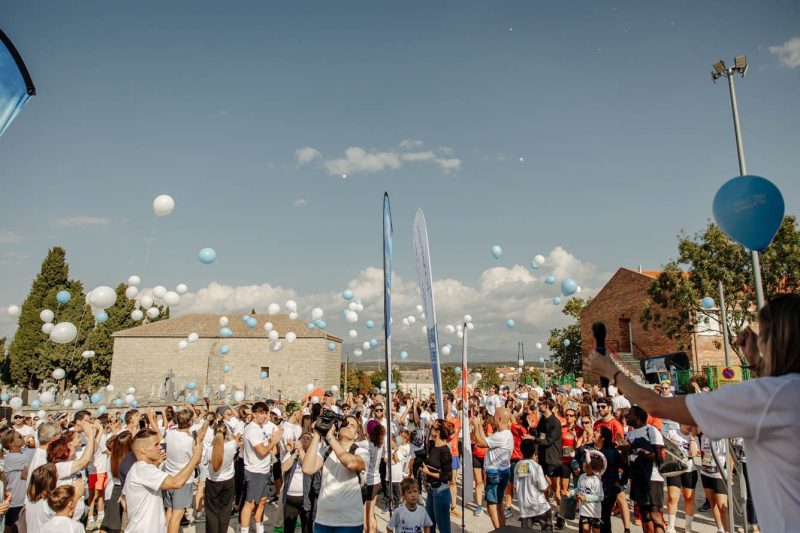 Una multitud de participantes en la carrera suelta globos blancos y azules al aire en un entorno al aire libre.