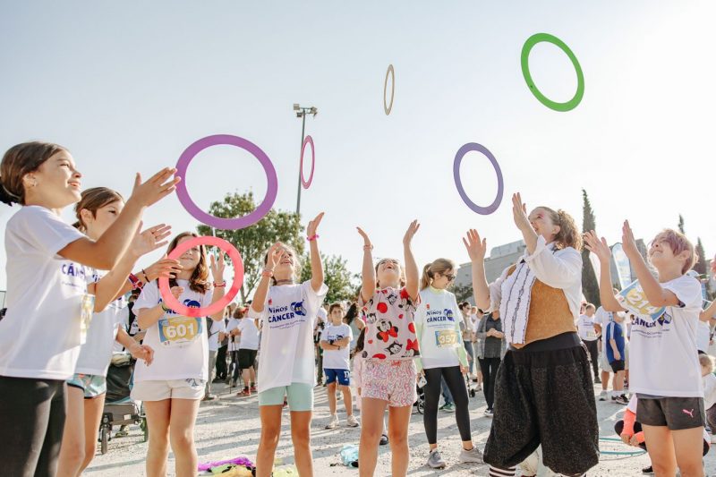 Niños participan en actividades de malabares con aros de colores en un espacio al aire libre durante un evento solidario.