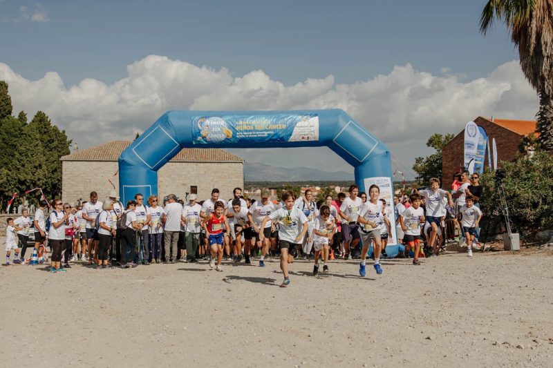 Corredores de todas las edades cruzan la línea de salida bajo un arco hinchable azul de la carrera solidaria.