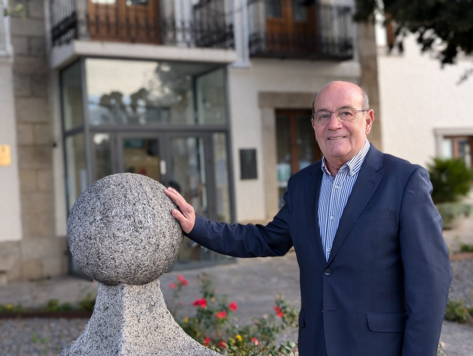 Antonio Vicente, alcalde de El Escorial, posa frente al Ayuntamiento con una mano apoyada sobre un adorno de piedra.