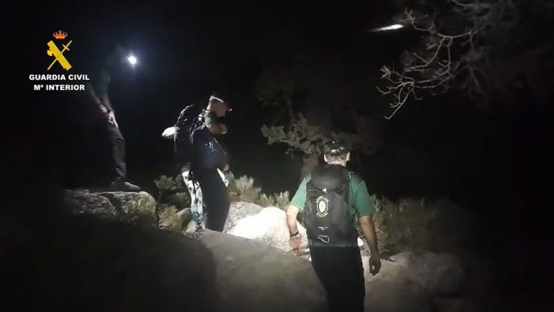 Efectivos del GREIM de la Guardia Civil guiando a personas rescatadas de noche en un terreno rocoso de montaña.