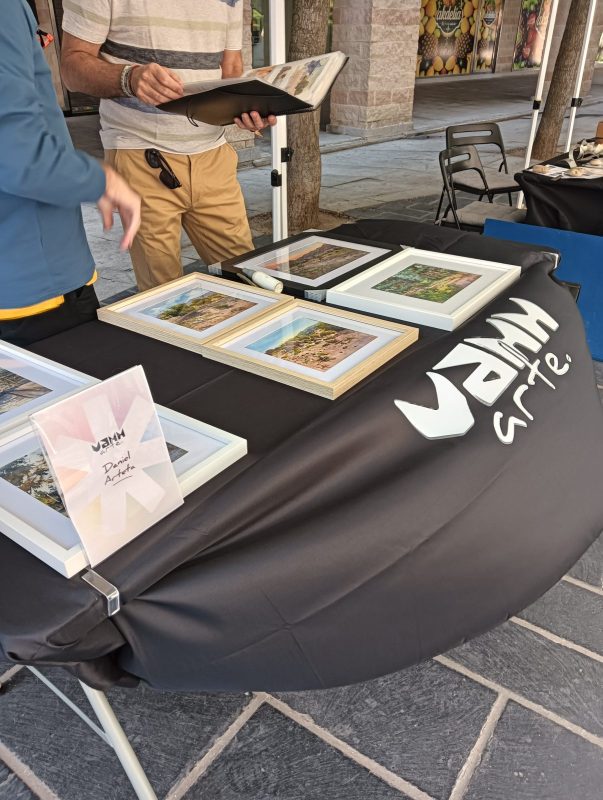 Dos personas revisan carpetas con obras artísticas expuestas en una mesa de la feria.