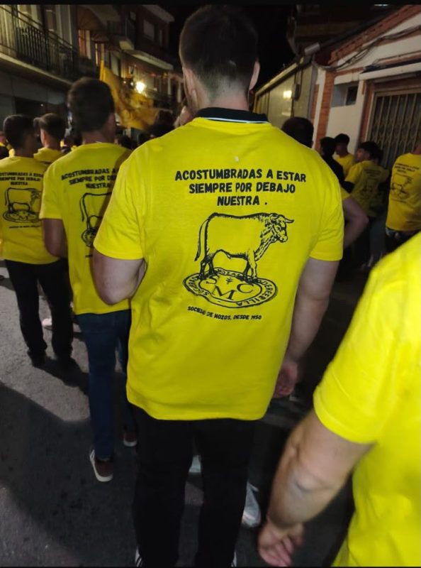 Espalda de mozos con camisetas amarillas que muestran el lema polémico y un dibujo taurino.