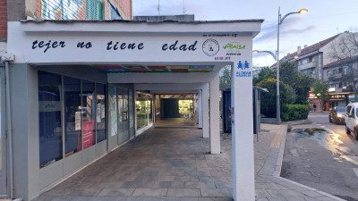 Soportales de un edificio de viviendas con el cartel "tejer no tiene edad" sobre la estructura.