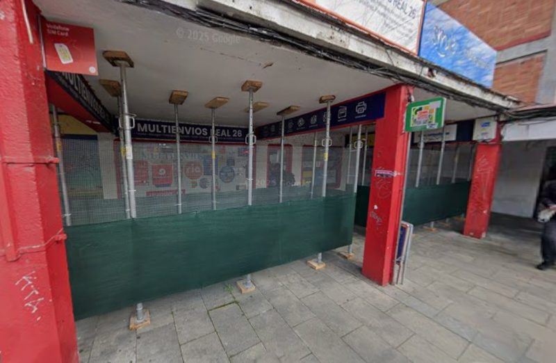 Soportales apuntalados con gatos metálicos y mallas verdes de obra frente a un local comercial.