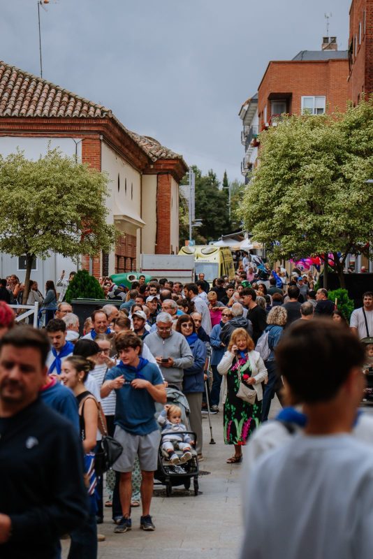 Numeroso grupo de personas paseando por una calle concurrida junto a edificios y árboles.