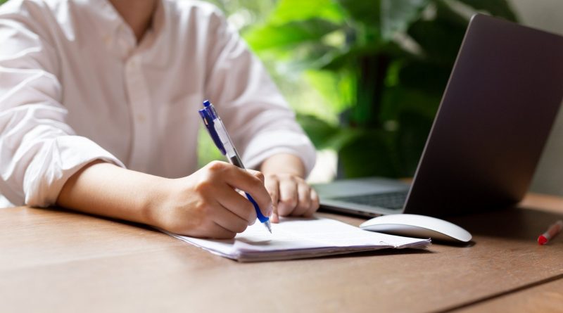 Hand filling document form contract with laptop an mouse on wooden table